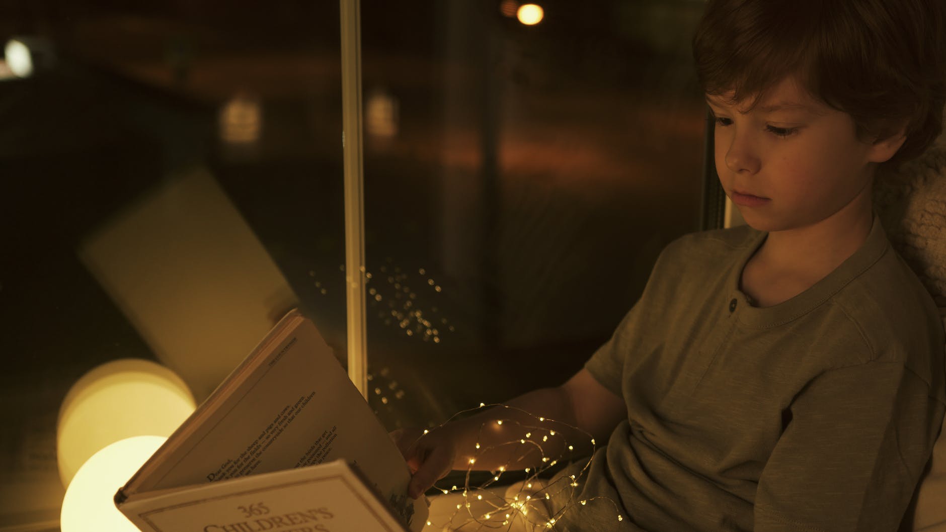 a boy reading a book near a window